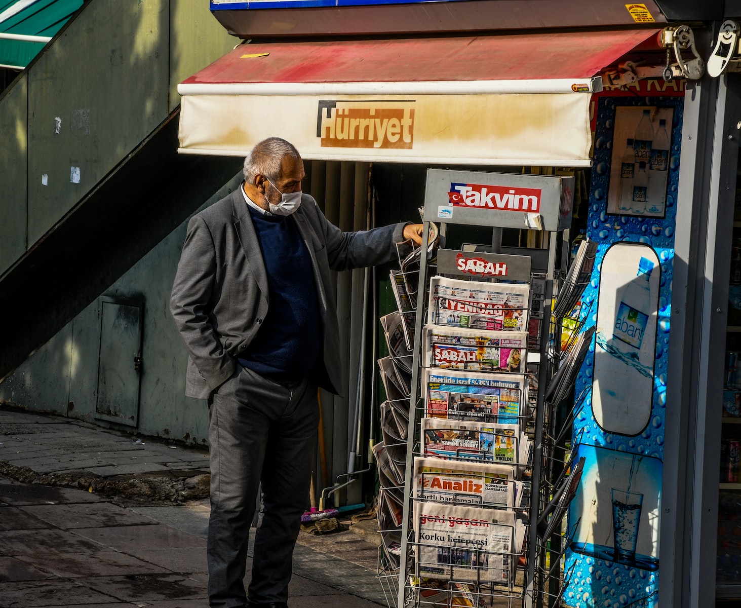 How do tabloid newspapers make money? man in black leather jacket and blue denim jeans standing beside red and white food stall